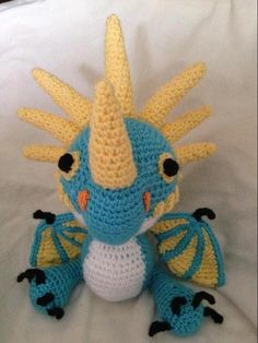 a crocheted blue and yellow dragon sitting on top of a white bed sheet