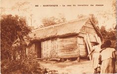 an old photo of two people standing in front of a small hut with thatched roof