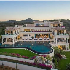 an aerial view of a house with a pool and lawn area at dusk, surrounded by mountains