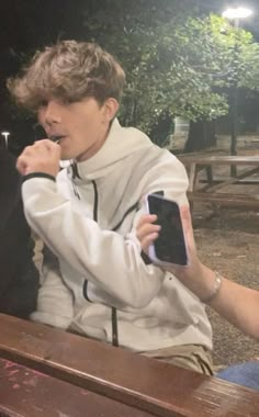 a man sitting on top of a wooden bench next to a woman holding a cell phone