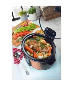 a crock pot filled with meat and vegetables on top of a table next to utensils