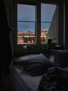 a bed sitting under two windows next to a window sill with city lights in the background