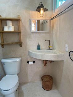 a white toilet sitting next to a sink in a bathroom under a light above it