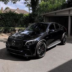 a black mercedes glc parked in front of a garage with trees and bushes behind it