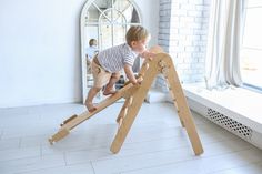 a toddler playing on a wooden ladder in a room with white walls and windows