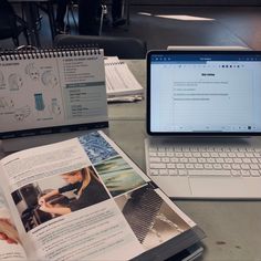 an open laptop computer sitting on top of a table next to a book and notebook