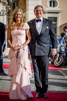 a man and woman in formal wear standing on a red carpet with motorcycles behind them