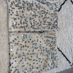 two pieces of fabric with silver sequins on them sitting on the floor next to a rug