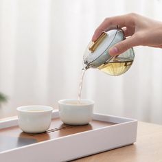 someone pouring tea into small cups on a tray