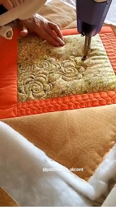 someone using a sewing machine to sew on an orange and gold quilted pillow