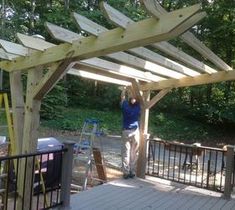 a man standing on top of a wooden deck under a pergolated roof next to a forest