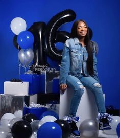 a woman sitting on top of a white box surrounded by balloons and presents in front of a blue background