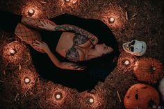 a woman laying on the ground surrounded by candles and pumpkins with her face painted