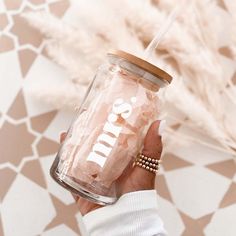 a person holding a glass jar with writing on it and a straw in the other hand