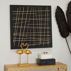 two gold flamingos stand on a table in front of a black painting