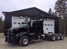 a black semi truck parked in front of a garage with two large tires on it's flatbed