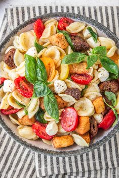 a bowl filled with pasta and vegetables on top of a striped table cloth next to a fork