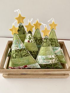 three small christmas trees in a wooden tray with gold stars on top and green fabric