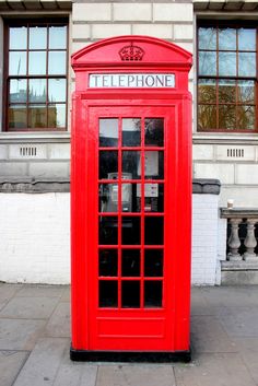 a red phone booth sitting on the sidewalk