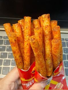 someone is holding some kind of food in front of a laptop computer and it looks like french fries