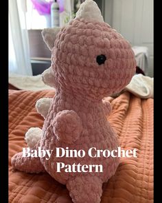 a pink crochet baby dino stuffed animal sitting on top of an orange bedspread