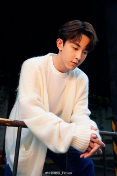 a young man sitting down wearing a white sweater