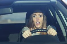 a woman driving a car with an surprised look on her face as she holds the steering wheel