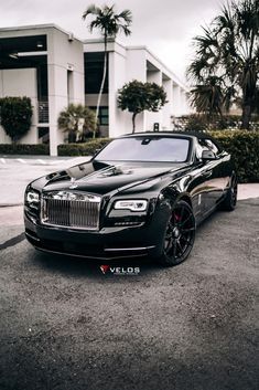 a black rolls royce parked in front of a building with palm trees on the side