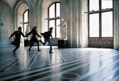 three people are dancing in an empty room with large windows and marble flooring on either side of them