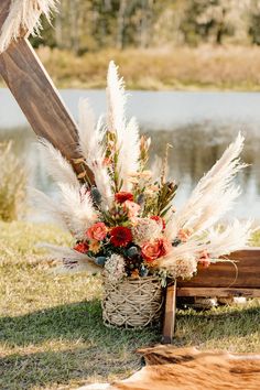 a basket filled with flowers sitting on top of a grass covered field next to a lake