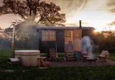 an outhouse with hot tub and chairs in the grass near trees at sunset or dawn