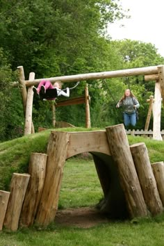 two women are playing in the park on swings and wooden structures made out of logs