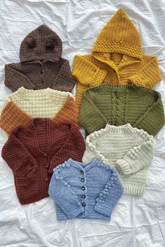 four knitted sweaters are laid out on a white sheet and one has a hood