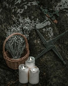 two white candles sitting on top of a rock next to a basket