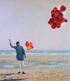 a man standing on top of a sandy beach flying a red and orange kite in the air