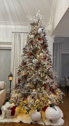 a white christmas tree with red and silver ornaments on it in a living room next to a couch