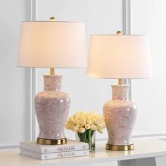 two lamps on a table with books and flowers in front of them, one is pink