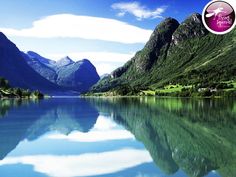 a lake surrounded by mountains and green trees with the sky reflecting in it's water