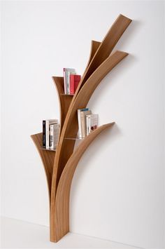 a wooden book shelf with books on it in the shape of a curved tree, against a white wall