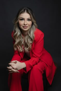 a woman in a red dress sitting on a chair with her arms crossed and looking at the camera