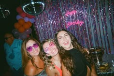 three girls are posing for the camera in front of balloons and streamers at a party