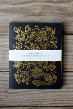 a black and gold pocket notebook sitting on top of a wooden table