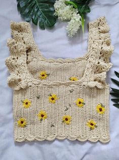 a crocheted sweater with sunflowers on the front and side, next to flowers