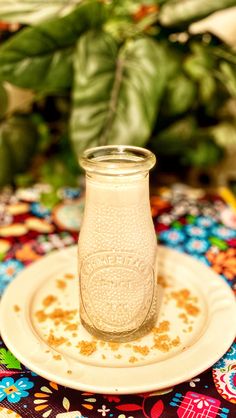 a small glass jar sitting on top of a white plate next to a green plant