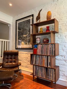 a brown leather chair sitting in front of a book shelf filled with vinyl record's