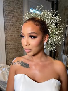 a woman in a white dress with flowers on her head and tattoos on her arm