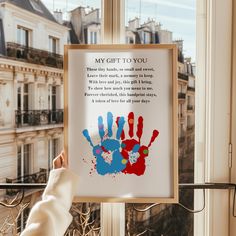 a person holding up a poster with their handprints in front of a window