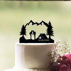 a wedding cake topper with a tent in the woods on it and flowers next to it