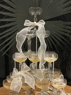 a table topped with lots of wine glasses filled with white liquid and decorated with bows