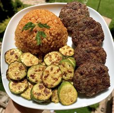 a white plate topped with meat, rice and zucchini on top of it